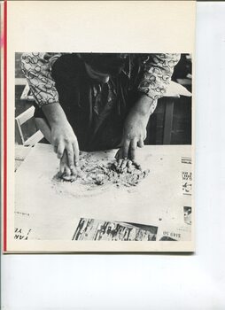 Child dressed in apron has their hands held as a teacher swirls them around a board moving a soft textured material