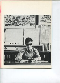 Teenage boy wearing dark glasses reading Braille in a classroom