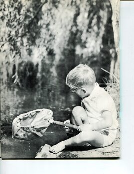 Young boy holds out a net as he sits beside a river
