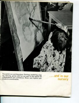 A young child uses a paint brush to create a picture in the classroom