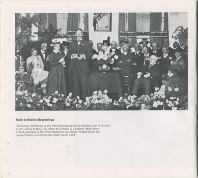 Photograph of Tilly Aston holding key to Commercial Road building, standing next to Senator G Fairbairn and surrounded by seated people on a stage