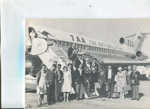 Blind cricketeers and supporters stand next to TAA jet holding shields and smiling for camera
