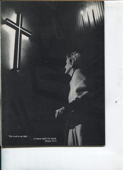 Elderly woman looks at a lighted Calvary cross with candles above her