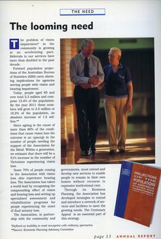 An older man acts as a sighted guide to another man along a corridor.