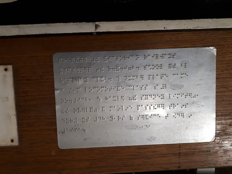 Braille metal plate on wooden sign