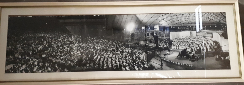 Black and white image of crowd, camera men and stage performers at Carols