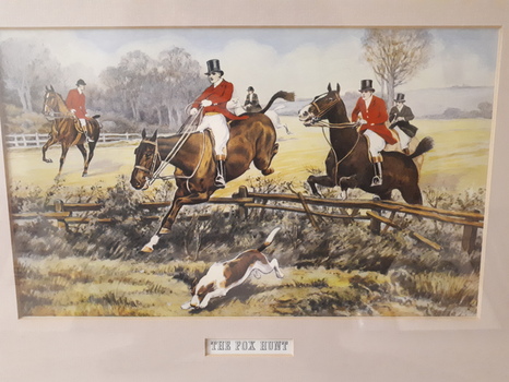 Men dressed in red coats and white shirts and jodhpurs jumping horses over fences following a hunting dog
