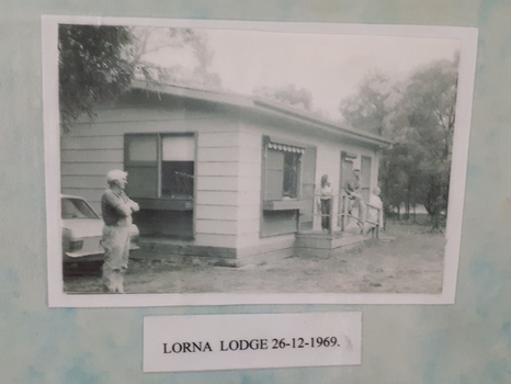 Three people standing around a weatherboard cottage