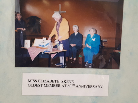 Elderly woman cuts decorated cake whilst three other women look on