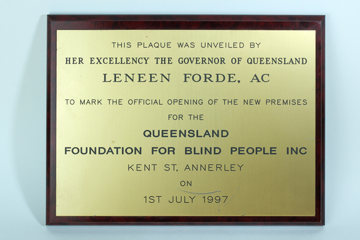 Gold coloured plate with black writing attached to dark brown board
