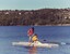 Woman holding two oars and a man balancing on the dual hull kayak