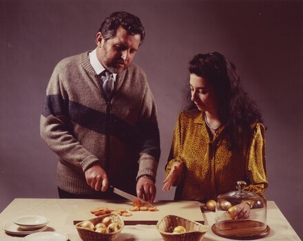 Man chopping carrots on a chopping board as a woman gestures