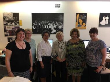 Six hard working woman stand in front of Black and White Ball memorabilia on wall behind them