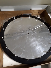 Large metal circle with raised markings and metal shafts around designated edge points. Two metal labels placed casually on top.