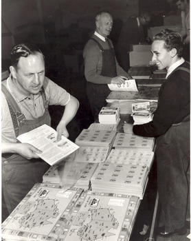 Three men work on an assembly line packaging booklets