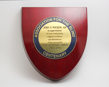 Red stained wood in shield shape with blue and gold plaque