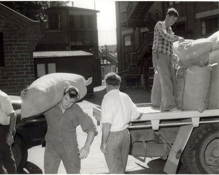 Three men unloading hessian sacks from a flat bed truck