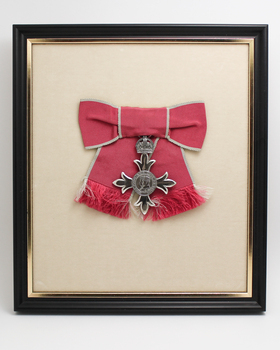 Silver medal is pinned to a red fabric ribbon with grey edging.