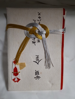 Envelope made of textured paper with origami, red edging, black writing and gold and silver ribbon
