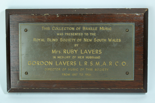 Metal plaque attached to dark brown painted wooden board