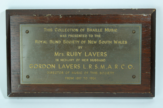 Metal plaque attached to dark brown painted wooden board