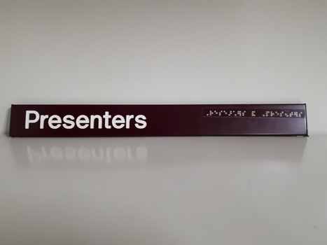 Dark red background with white letters and braille tape on top right side