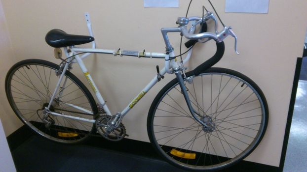 White mens bicycle held upright by a bracket on a wall