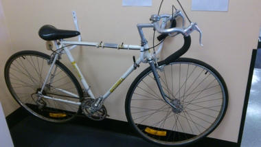 White mens bicycle held upright by a bracket on a wall