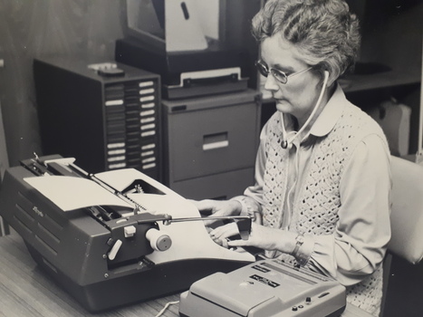 Female listens to dictaphone and transcribes sounds on to a typewriter