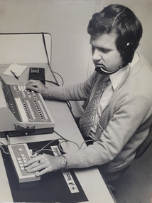 Man wearing headphones and using telephone exchange as well as another machine