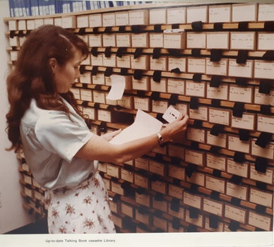 Woman removes cassette from drawer and checks it against paper in her hand