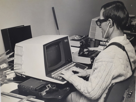 Man wearing a Sonic Guide types on a computer with an Opticon beside him