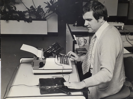 Man sits in front of typewriter with device attached, places his hand on a Opticon