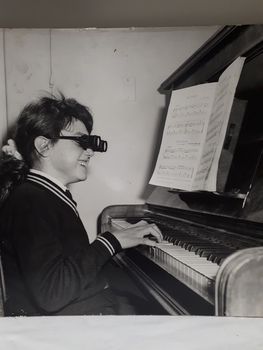School girl playing upright piano wearing a pair of binocular glasses