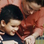A woman assists a boy cut his hot dog on a plate. 