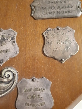 Wooden shield with smaller silver plates engraved with winner names and round wooden ball top in middle with two mini white canes