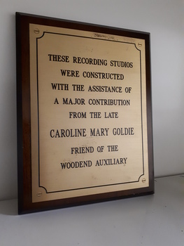 Gold coloured plate with black writing on wooden rectangle