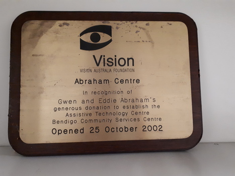 Black writing on gold coloured sheet attached to wooden plaque