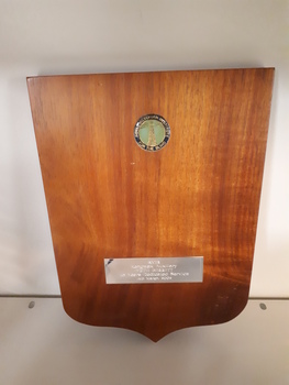 Wooden shield with enamel badge at top and metal plaque near base
