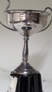 Rear view of silver cup with two handles on black base with years and winner engraved