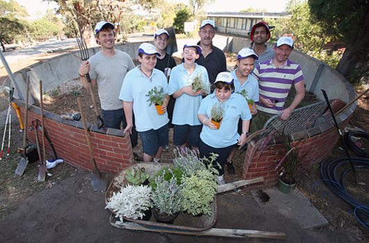 Five adults stand behind school children holding plants.