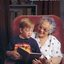 Mary Longman smiles as she holds a magnifier and listens to her grandson Andrew speak about a storybook, whilst holding him on her lap.
