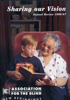 Mary Longman smiles as she holds a magnifier and listens to her grandson Andrew speak about a storybook, whilst holding him on her lap.
