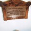 Wooden plaque with an elderly man seated below it.