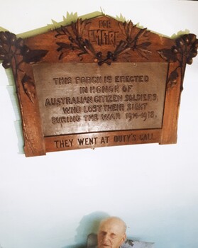 Wooden plaque with an elderly man seated below it.