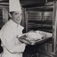 Male in chef uniform places a tray into the oven
