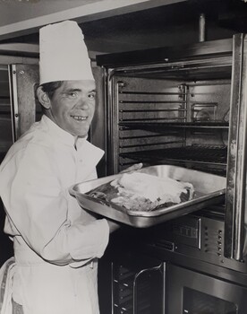 Male in chef uniform places a tray into the oven
