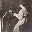 Woman in neck to floor dress, using a Braille shorthand machine in a room filled with books.