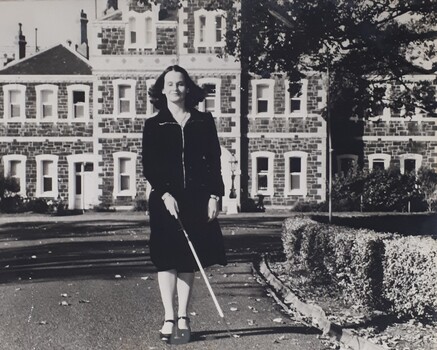 Female using white cane to walk along driveway outside RVIB building