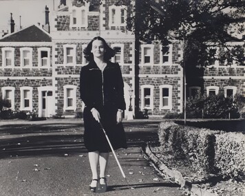 Female using white cane to walk along driveway outside RVIB building